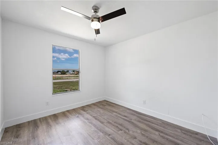Room with wood-finish flooring, white baseboards, and bright white walls