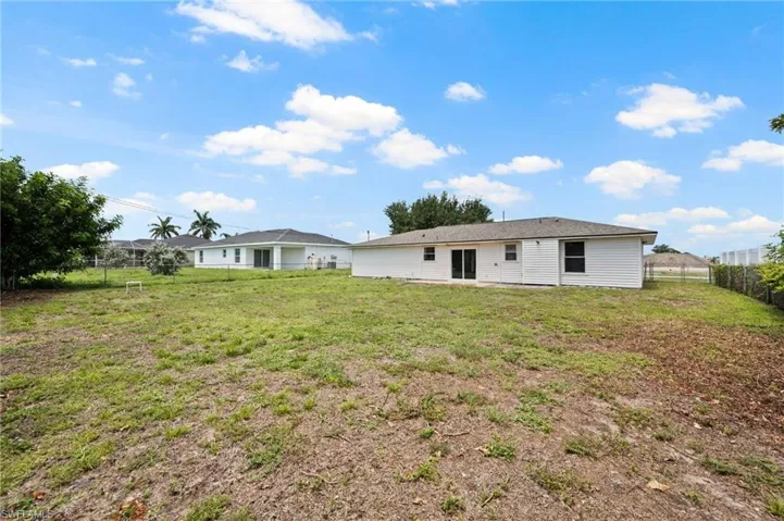 Expansive rear yard featuring a partial chain-link fence, mature trees, and direct access to the main structure via sliding glass doors
