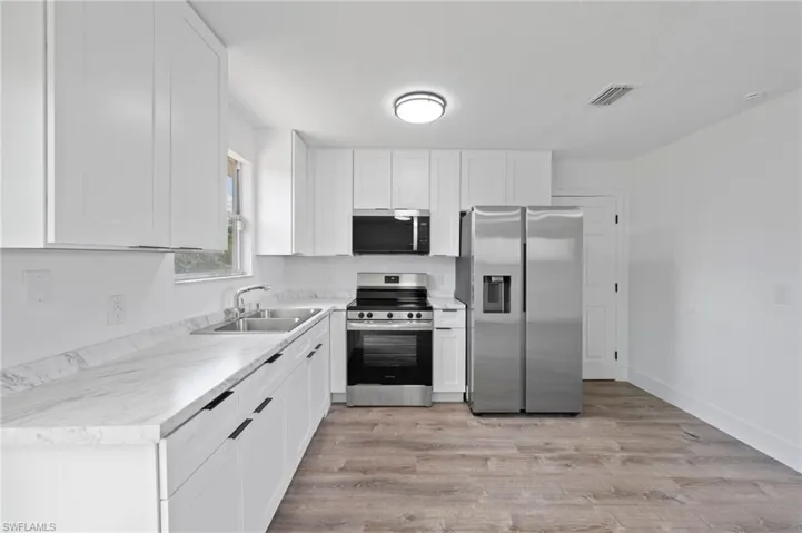 Modern kitchen featuring white shaker cabinetry, stainless steel appliances, marble-look countertops, a double basin sink, and wood-finish flooring