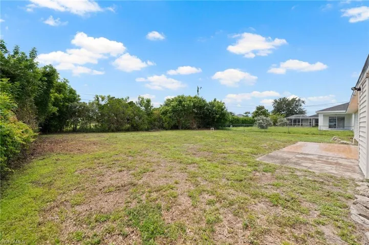 Expansive rear yard featuring a grass lawn, mature perimeter landscaping, and a concrete patio pad