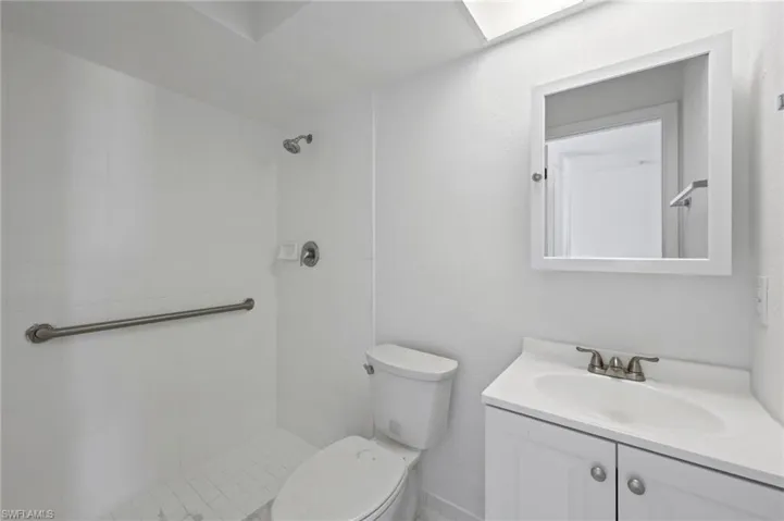 White tiled shower with a grab bar, featuring a chrome shower head and controls