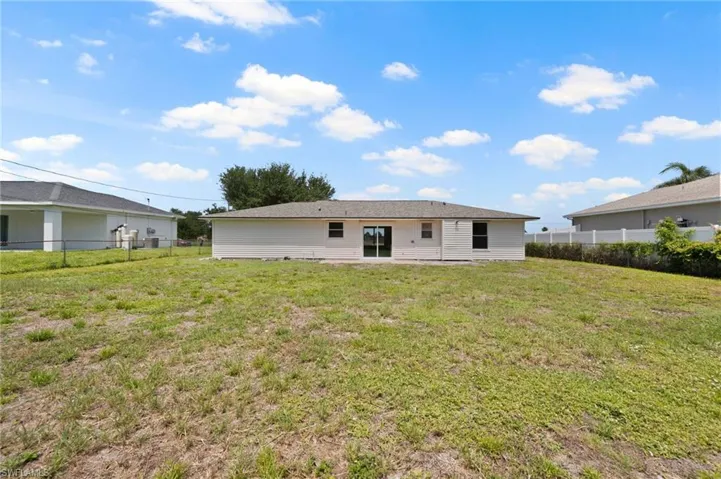 Expansive grassy yard area with a single-story residence featuring a light-colored exterior finish