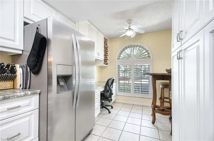 Kitchen with white cabinetry, stainless steel fridge, light tile patterned floors, a textured ceiling, and a desk