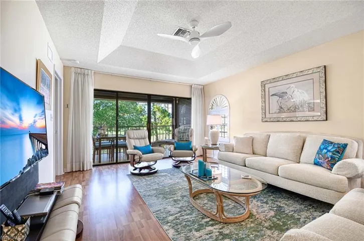 Living room featuring wood finished floors, a raised ceiling, ceiling fan, and a textured ceiling