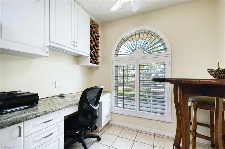Office space with built in study area, a textured ceiling, light tile patterned floors, and ceiling fan