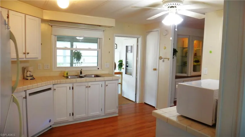 Kitchen featuring sink, tile counters, dishwasher, light hardwood / wood-style floors, and white cabinets