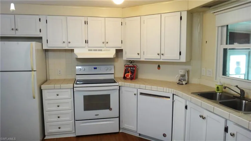 Kitchen featuring white cabinetry, sink, backsplash, tile counters, and white appliances