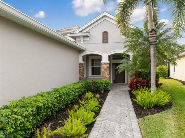 Property entrance with stucco siding, stone siding, a tile roof, and a lawn