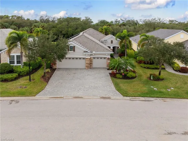 View of front facade with a front yard, decorative driveway, a garage, stone siding, and a tiled roof