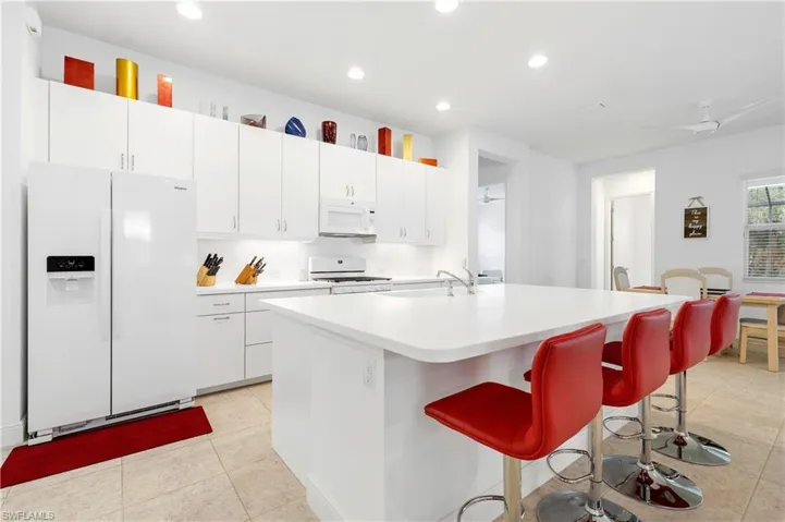 Kitchen with white appliances, white cabinetry, ceiling fan, light countertops, and a center island with sink