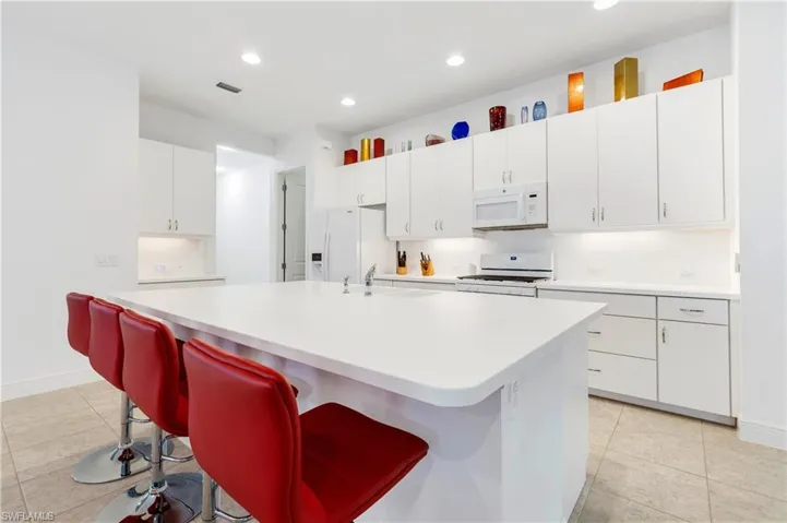 Kitchen with white cabinets, white appliances, a kitchen breakfast bar, light tile patterned flooring, and recessed lighting