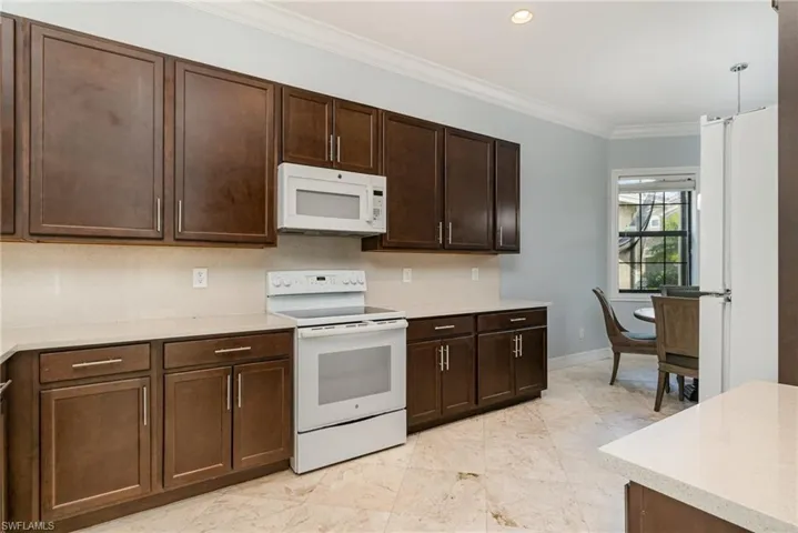 Kitchen with white appliances, dark wood finish cabinetry, crown molding, recessed lighting, and light stone countertops