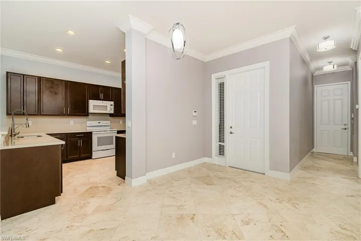 Kitchen featuring dark wood finish cabinets, white appliances, ornamental molding, decorative light fixtures, and light stone counters