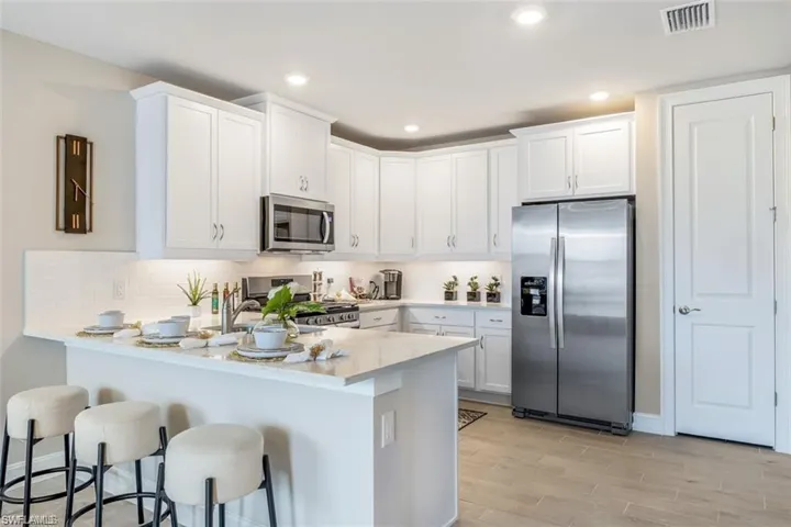 Kitchen featuring light wood-type flooring, white cabinetry, a kitchen breakfast bar, backsplash, and appliances with stainless steel finishes