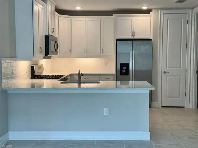 Kitchen with appliances with stainless steel finishes, kitchen peninsula, sink, and white cabinets
