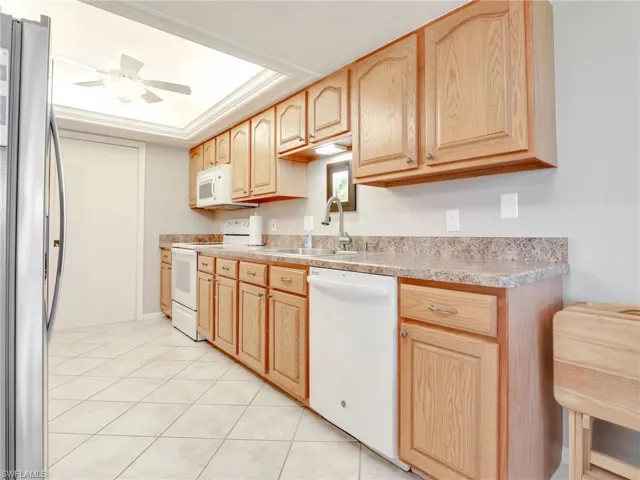 Kitchen with sink, light tile patterned flooring, light brown cabinetry, white appliances, and ceiling fan