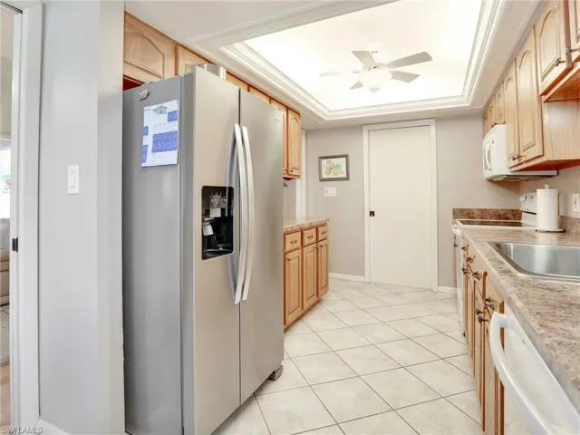 Kitchen with ceiling fan, light tile patterned floors, light brown cabinetry, a tray ceiling, and white appliances