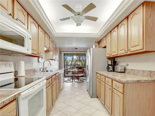 Kitchen with light brown cabinets, sink, pendant lighting, light tile patterned floors, and white appliances