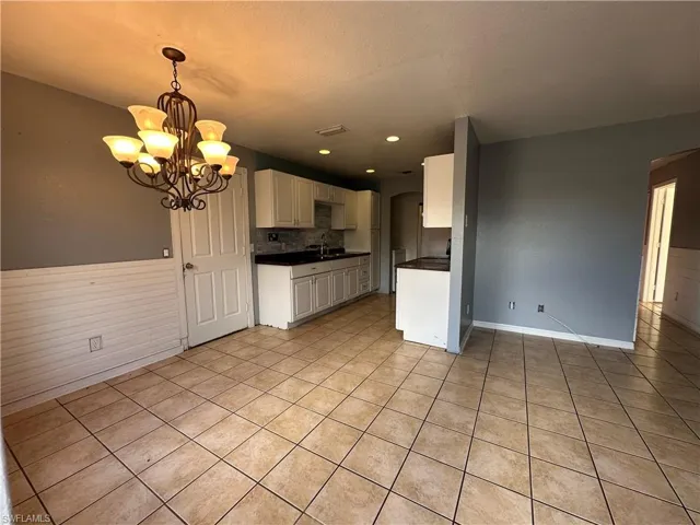 Kitchen with light tile patterned flooring, a notable chandelier, hanging light fixtures, sink, and white cabinets