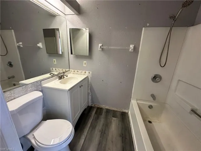 Full bathroom with toilet, hardwood / wood-style flooring, vanity, shower / tub combination, and a skylight