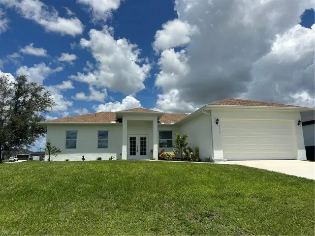 View of front of house featuring french doors, stucco siding, a front lawn, and driveway
