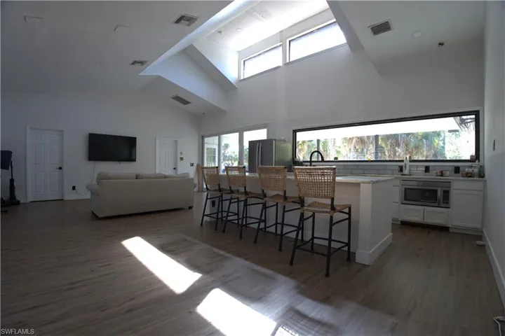 Kitchen featuring white cabinetry, a kitchen bar, a towering ceiling, a kitchen island with sink, and appliances with stainless steel finishes