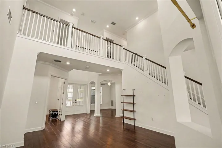 VIEW SHOWING THE SOARING CEILING AND STUNNING STAIRCASE TO 3 BEDROOMS AND BONUS ROOM.  DEN IS SHOWN JUST TO LEFT OF ENTRY DOORS.  DINING AREA IS BY ARCHES.  AT FAR LEFT IS ENTRANCE TO PRIMARY SUITE.