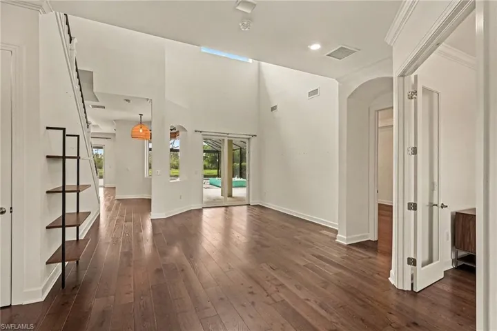 VIEW INTO LIVING ROOM AREA.  DEN'S WOOD-FRAMED FRENCH DOORS SHOWN AT RIGHT.  ENTRANCE TO PRIMARY SUITE IS JUST BEYOND THAT.  SLIDING DOORS LEAD TO OUTDOOR LIVING AREA.  BREAKFAST NOOK SHOWN AT REAR LEFT.  DOOR TO FAR LEFT IS TO STORAGE, UNDER THE STAIRCASE.
