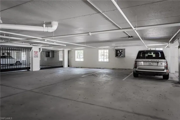 Secure covered parking garage featuring concrete flooring, a white painted ceiling with exposed piping, and a gated entry system