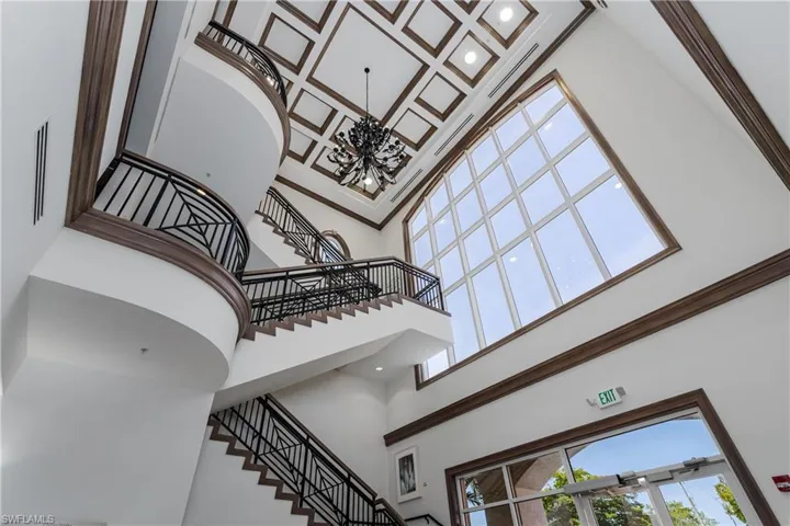 Grand foyer featuring a coffered ceiling, multi-level staircase with decorative wrought iron railings, and a prominent arched window wall