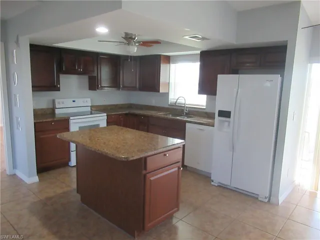 Kitchen featuring white appliances, sink, a center island, ceiling fan, and light tile patterned floors