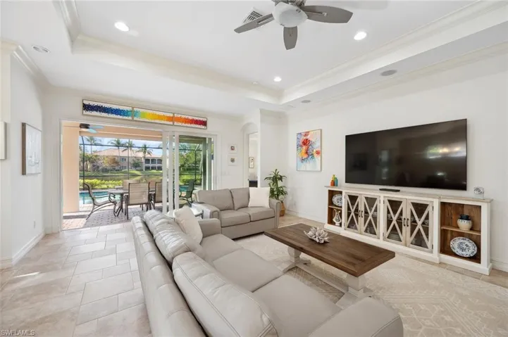Tiled living room featuring ceiling fan, ornamental molding, and a tray ceiling