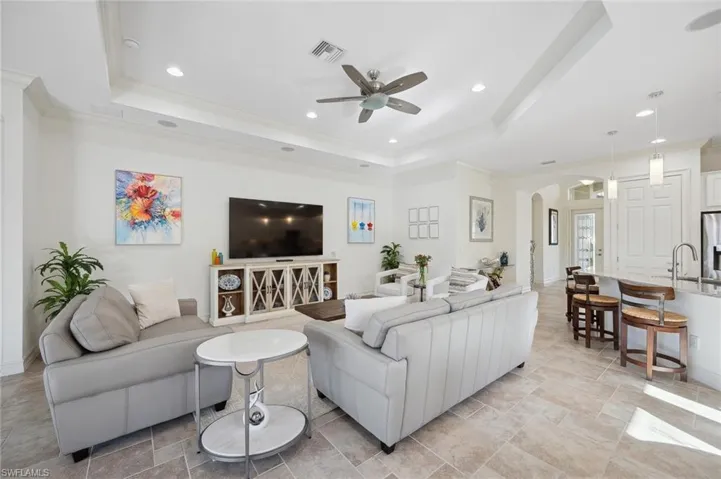 Living room featuring a raised ceiling, ceiling fan, and crown molding
