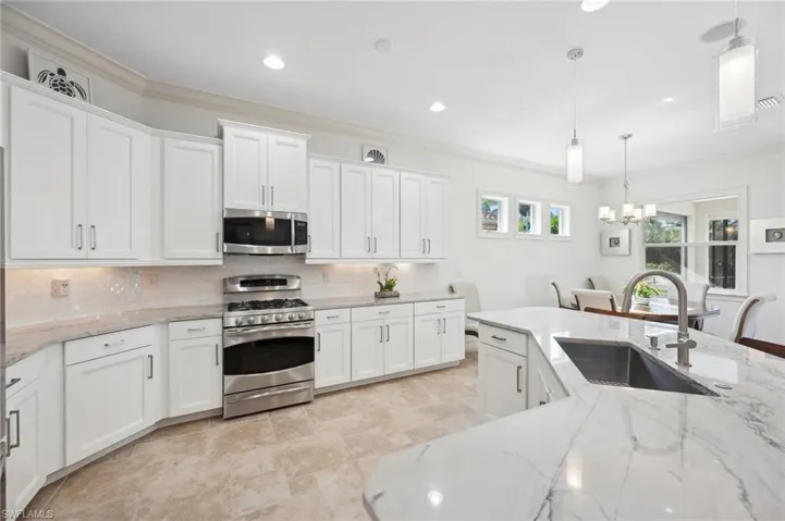 Kitchen with hanging light fixtures, white cabinetry, sink, and stainless steel appliances