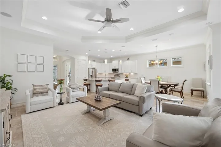 Living room featuring a tray ceiling, light tile patterned floors, ceiling fan with notable chandelier, and ornamental molding