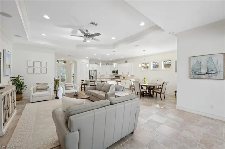 Living room with a tray ceiling, crown molding, and ceiling fan with notable chandelier