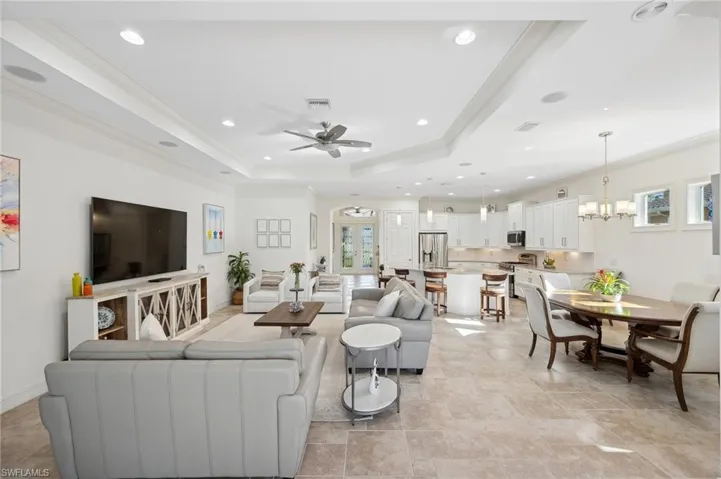 Living room with ceiling fan with notable chandelier, a raised ceiling, and crown molding