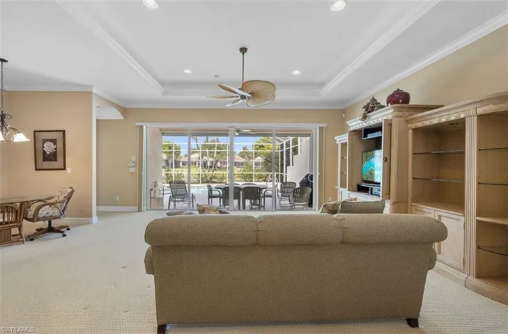 Living room featuring crown molding, carpet floors, ceiling fan with notable chandelier, and a raised ceiling