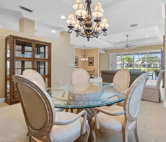 Dining space with a raised ceiling, light carpet, ornamental molding, and a chandelier