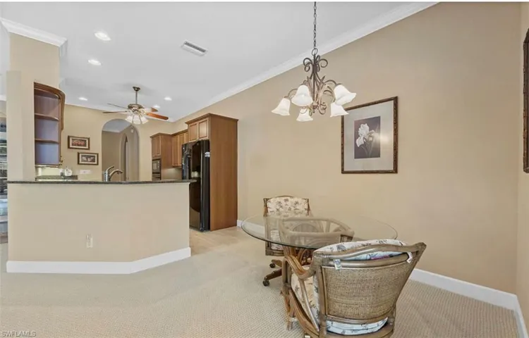Dining space with ceiling fan with notable chandelier, light carpet, sink, and ornamental molding
