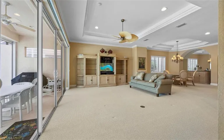 Carpeted living room featuring ornamental molding, a tray ceiling, and ceiling fan with notable chandelier