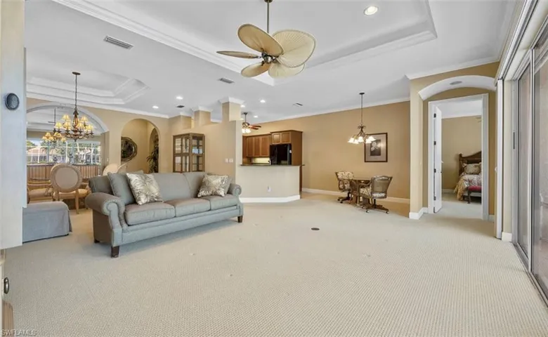 Carpeted living room with a tray ceiling, ornamental molding, and ceiling fan with notable chandelier