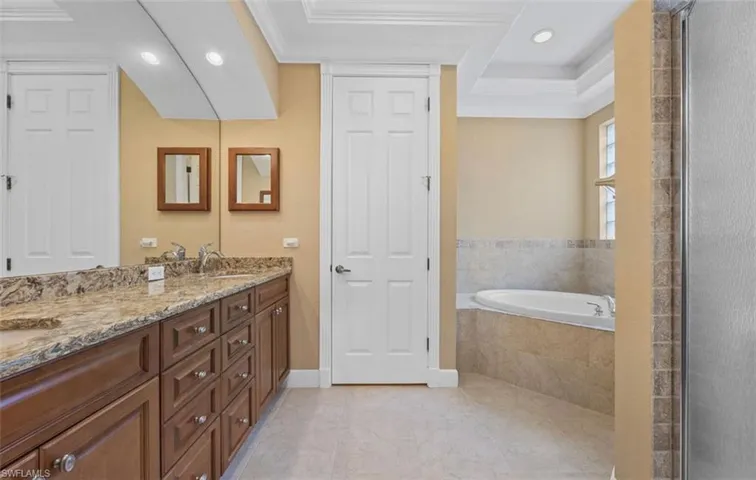 Bathroom featuring a tray ceiling, vanity, tile floors, tiled bath, and ornamental molding