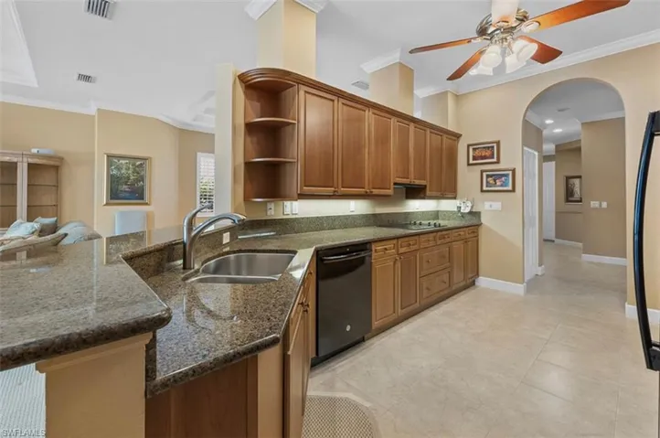 Kitchen featuring ceiling fan, black appliances, dark stone countertops, light tile floors, and sink