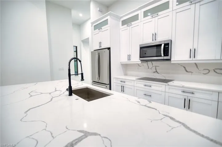 Kitchen featuring glass fronted cabinets, white cabinets, and light stone countertops