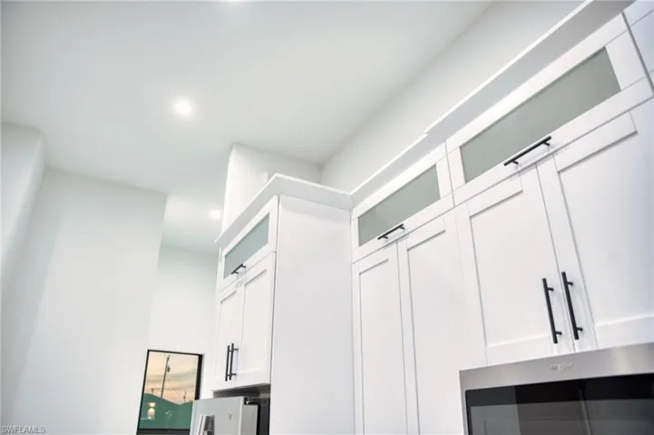 Kitchen view of white cabinets, glass insert cabinets, stainless steel microwave, and recessed lighting