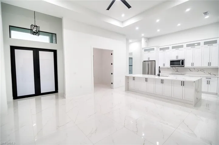 Kitchen featuring glass fronted cabinets, white cabinetry, a high ceiling, a spacious island, and light stone countertops