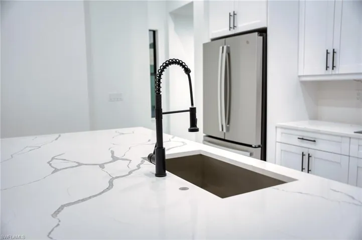 Kitchen view of freestanding refrigerator, white cabinetry, and light stone countertops