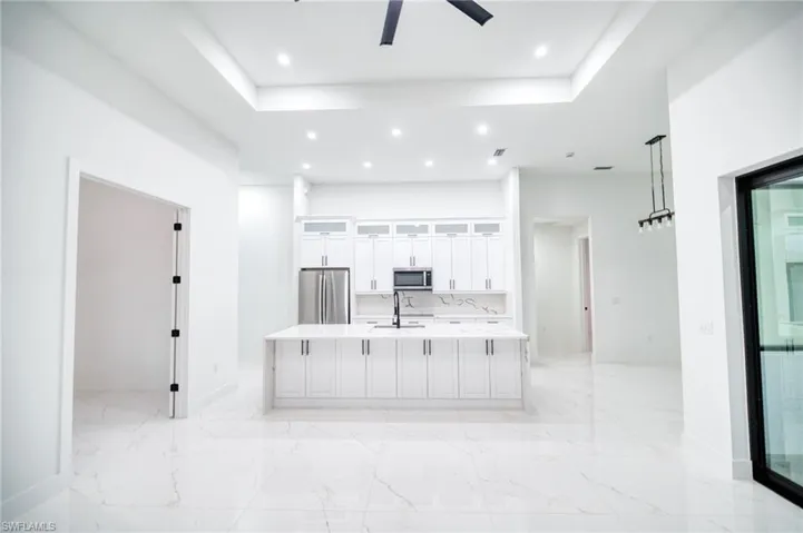 Kitchen with white cabinets, a large island with sink, glass fronted cabinets, a tray ceiling, and light stone counters