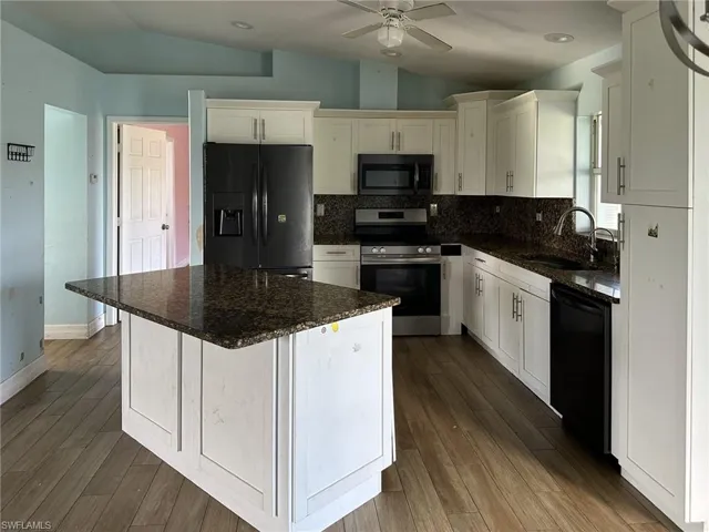 Kitchen featuring an island with a granite countertop, white cabinetry, dark stone backsplash, and wood-finish flooring